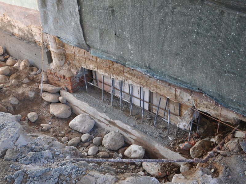 Excavated foundation with reinforcement bars installed during underpinning a wall to stabilise structure.