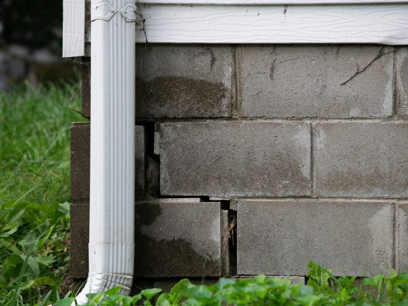 Cracked concrete block wall beneath a home, showing damage that may require underpinning house foundation repairs.