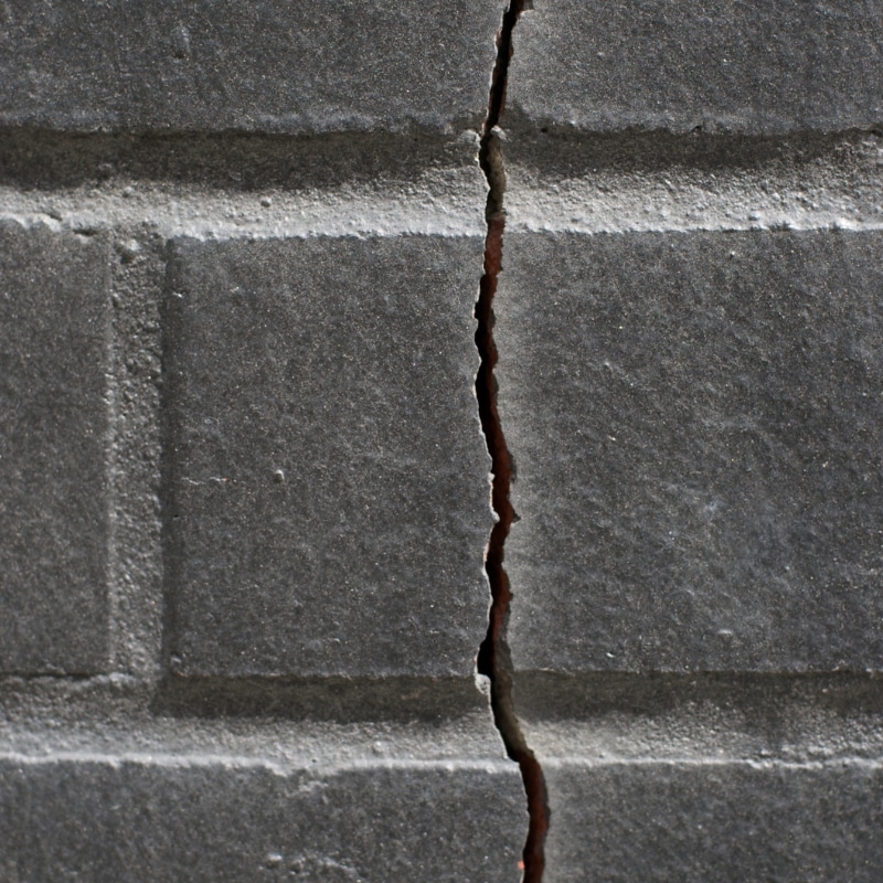 Foundation problems shown by a vertical crack running through a concrete block wall surface.